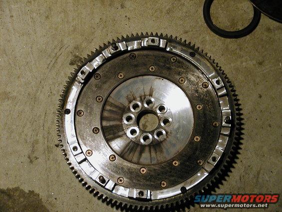 Close-up of a car flywheel with a toothed outer edge, resting on a concrete floor