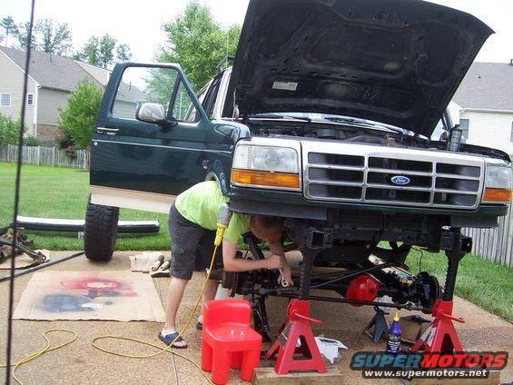 Green 1992 Ford Bronco with hood open, front end on jack stands, person working underneath