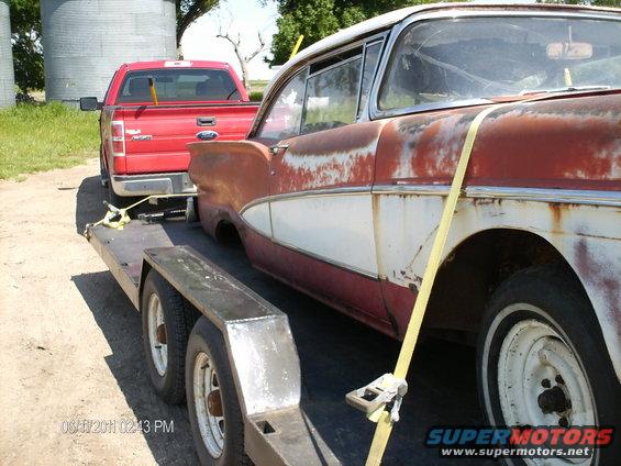 Red pickup truck towing a rusty 1957 Ford car on a trailer