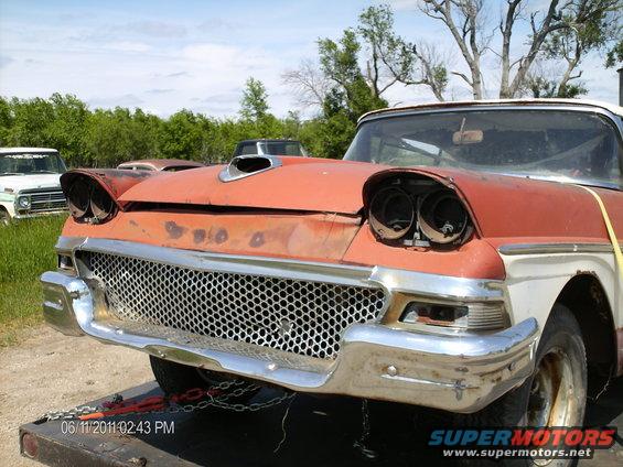 Orange and white 1958 Ford Fairlane with a custom hood scoop and missing headlights, viewed from the front