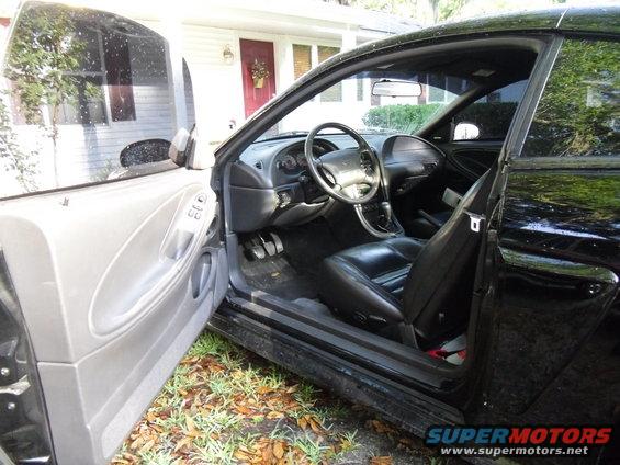 Black interior of a car with driver's side door open, showing dashboard, steering wheel, and seats