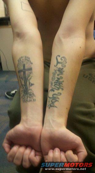 Two arms with tattoos: one of a cross with text, the other with script text