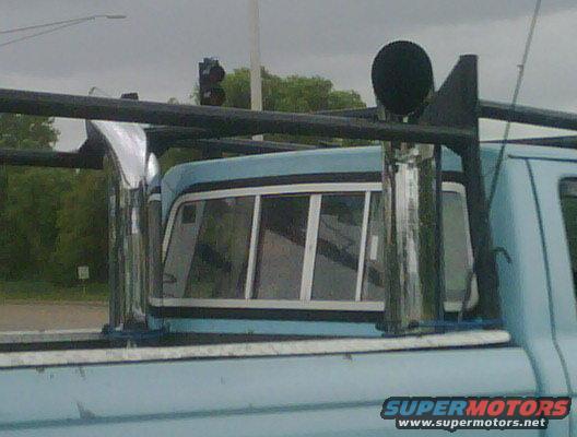 Light blue pickup truck cab rear window and side, with a black rack and chrome exhaust stacks. Supermotors.net logo visible