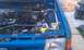 1991 Ford Festiva - The engine bay of a blue vehicle is shown, the battery and various hoses. A Supermotors.net logo is present.