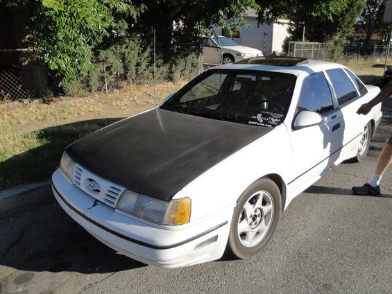 White sedan with a black hood, sunroof, and aftermarket wheels parked on a street