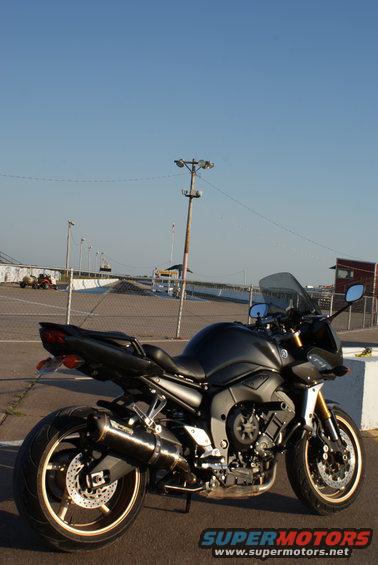 Black motorcycle parked at a drag strip. Some lights and a small building in the background