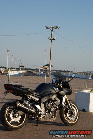 Black 2008 Yamaha FZR1000 motorcycle parked on asphalt, with a racetrack in the background