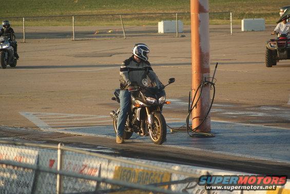 Motorcycle rider in helmet and jacket on a bike at a drag strip, another motorcycle and an ATV visible