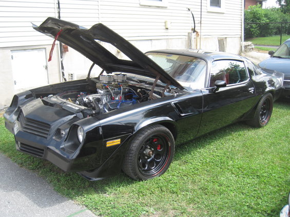 Black muscle car with hood open, showing engine. Aftermarket wheels and red brake calipers visible