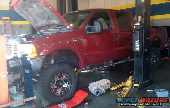 Red pickup truck with hood up on a lift, transmission removed