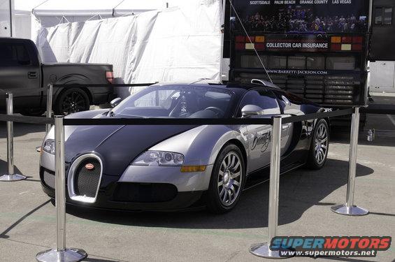 Bugatti Veyron with a black hood and roof, parked behind stanchions. A Ford pickup is behind it