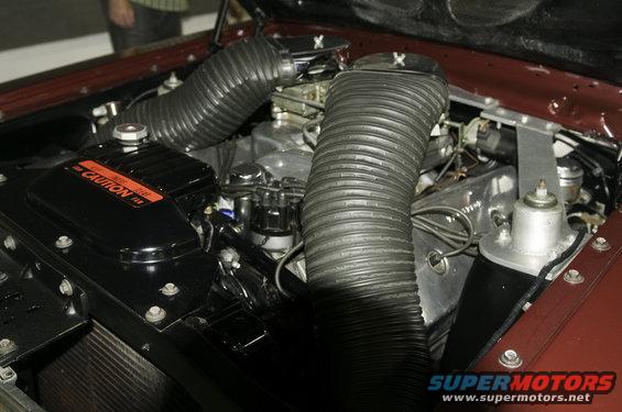 Engine bay showing dual carburetors, black air intake hoses, and a black cover with orange 'CAUTION' text