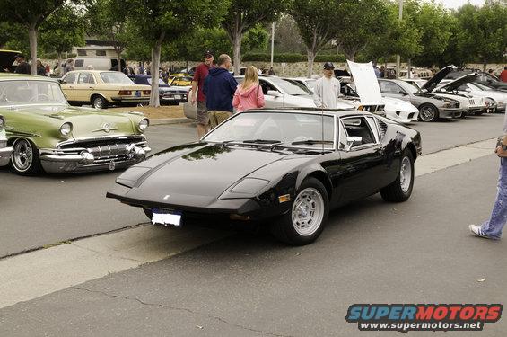 Black De Tomaso Pantera parked on asphalt with other cars and people around
