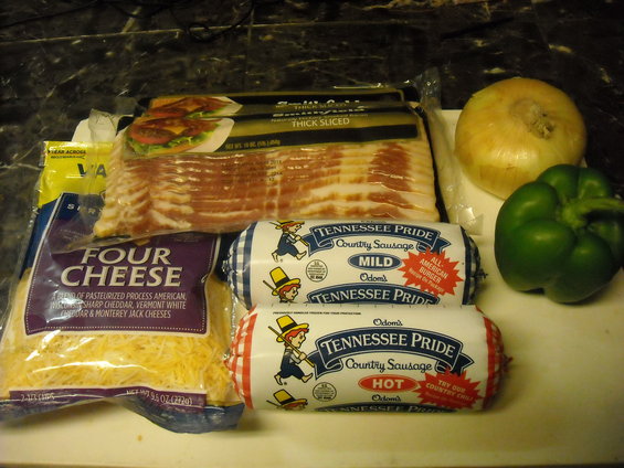 Packaged bacon, shredded cheese, two sausage rolls, an onion, and a green bell pepper