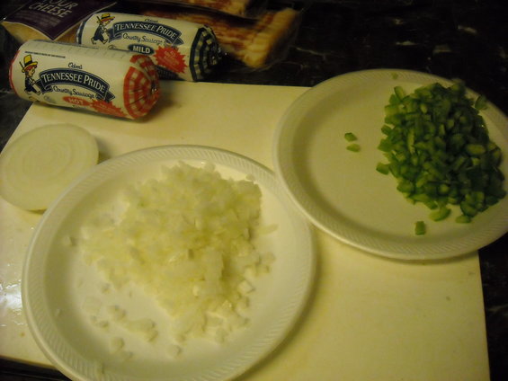 Chopped onions, green peppers, and sausage rolls on a cutting board