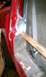 1994 Ford F-250 - Close-up of a vehicle's red body panel undergoing repair, showing fresh welds and a rusty pipe.