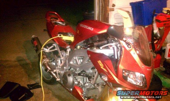 Red motorcycle with exposed engine and yellow wire. Suzuki logo visible