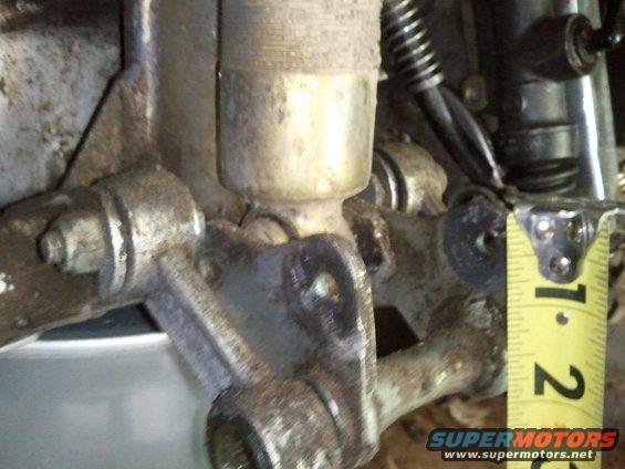 Close-up of a rusty suspension component with a yellow tape measure indicating 1-2 inches