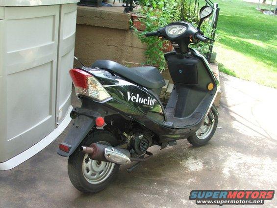 Black scooter parked next to a storage unit. Has 'Velocity' text on the side