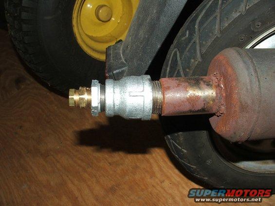 Close-up of a custom exhaust pipe with a brass fitting attached to a rusty metal pipe, next to a scooter tire and yellow wheel