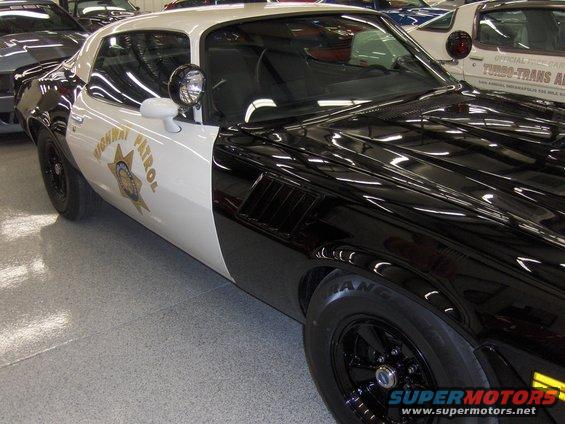 Black and white police car with "HIGHWAY PATROL" text and badge on door. Appears to be a 1977 Chevrolet Camaro