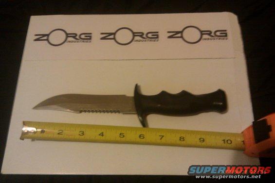 Knife next to a measuring tape, with Zorg Industries logo in background