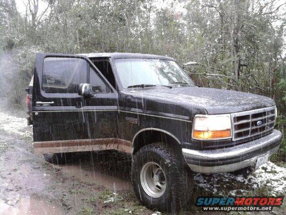 1994 Ford Bronco with driver's door open, stuck in muddy terrain during rain