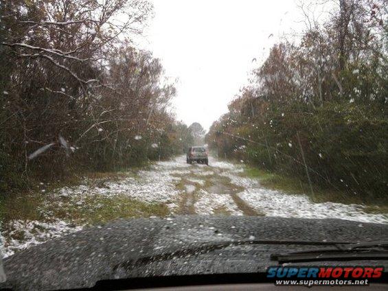 SUV driving on snowy dirt road, trees on sides