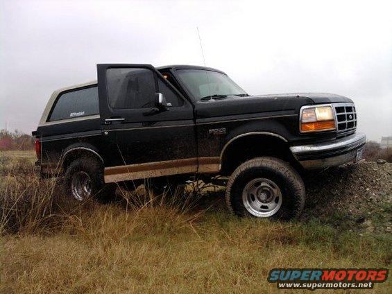 Black Ford Bronco with tan top, driver door open, on grassy terrain