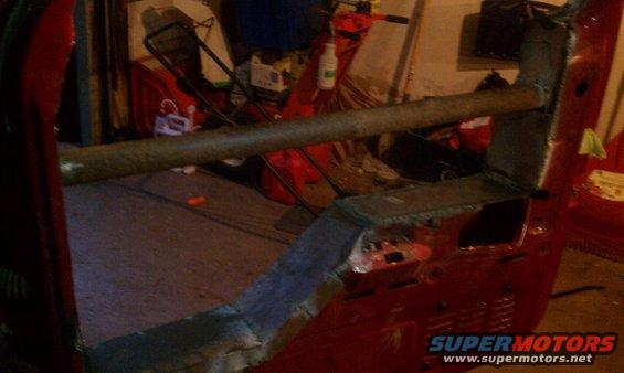 Interior of a red vehicle, possibly a truck cab, with a metal roll bar installed. The floor is covered with a dark mat