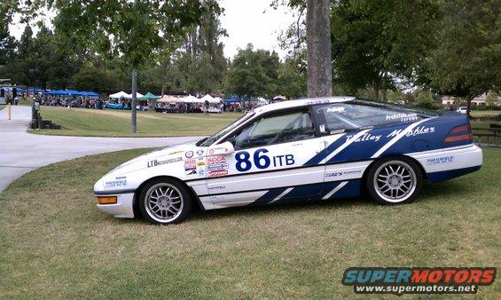 White and blue 1990 Ford Probe race car with number 86 ITB, parked on grass