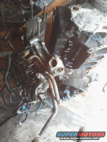 Engine block with hoses and wiring attached, sitting on a wooden surface