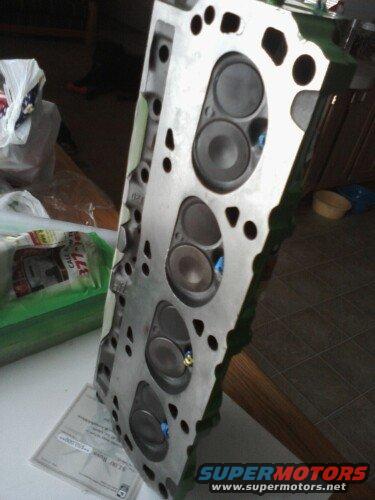 Engine cylinder head with visible valves and ports, resting on a table