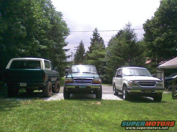 Green 1979 Ford Bronco with white top, lifted suspension, and large tires, parked next to two other SUVs