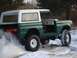 1974 Ford Bronco - A green and white 1974 Ford Bronco with its doors removed drives through the snow.
