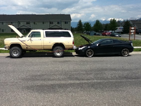 Beige pickup truck towing black coupe, both with hoods open