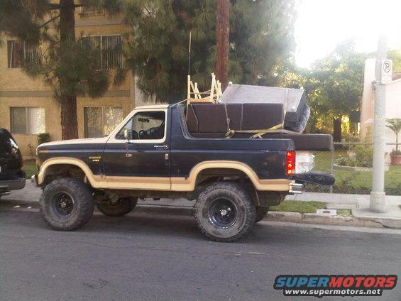 Side view of a lifted 1986 Ford Bronco carrying furniture strapped to the roof and in the bed