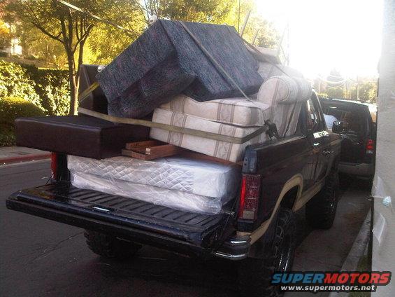 Dark brown Ford Bronco loaded with furniture and mattresses, viewed from the rear