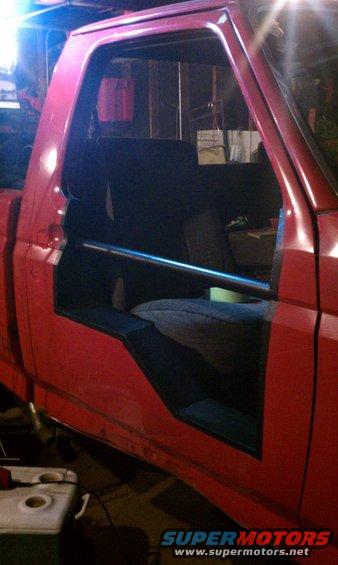 Red pickup truck interior with roll bar, door removed, showing seats and dashboard