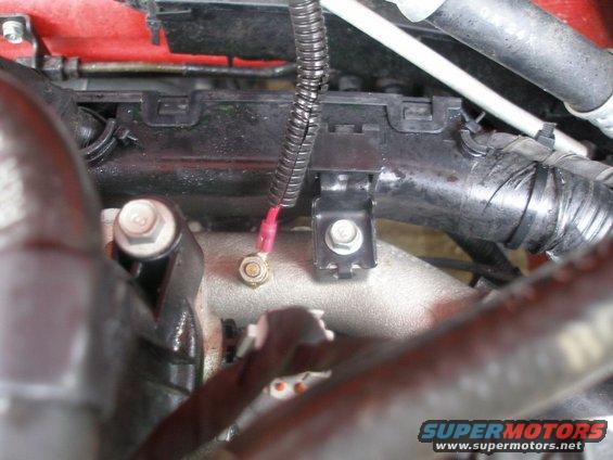 Engine bay wiring harness with a red wire connected to a ground point via a bolt and nut