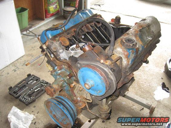 V8 engine on an engine stand, with a toolbox nearby. Engine is rusty and has blue painted components