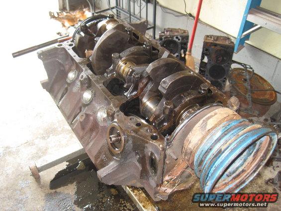 Engine block with crankshaft and connecting rods visible. Two cylinder heads are in the background
