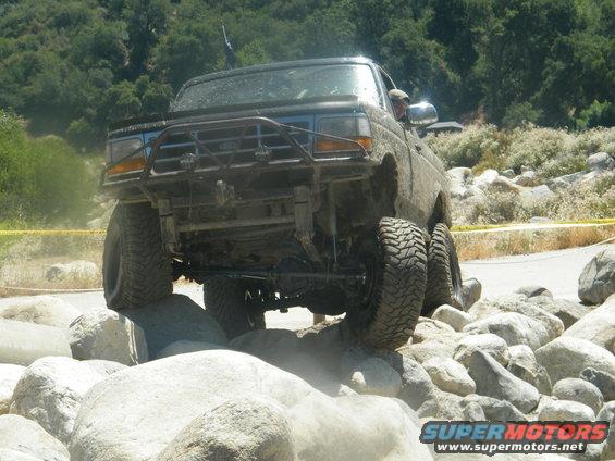 Front view of a lifted off-road vehicle with a bull bar, climbing over large rocks