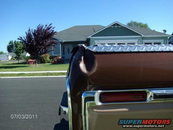 Close-up of a brown truck bed with a diamond plate toolbox on top. House and tree in background