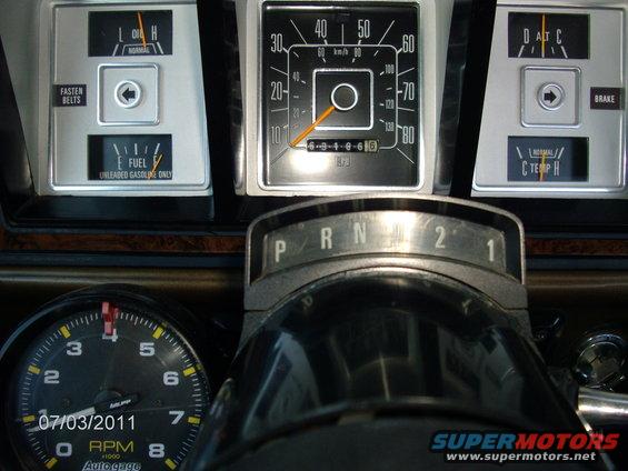 Interior view of dashboard gauges including speedometer, fuel, oil, temp, and tachometer. Gear selector shows P, R, N, 2, 1