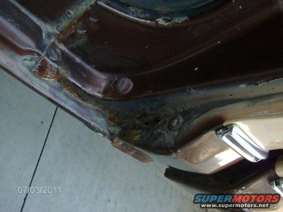 Brown vehicle door jamb with significant rust and damage. Chrome door handle visible