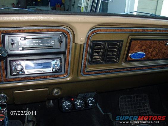 Dashboard with wood grain trim, aftermarket stereo, and climate controls. Also has a Ford emblem and auxiliary gauges