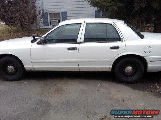White sedan parked on pavement in front of a house. Shows side profile of the car