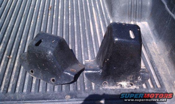 Two black metal brackets with mounting holes, resting on a ribbed surface