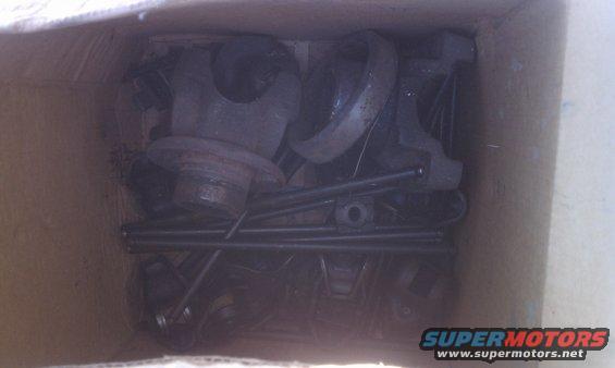 Box of assorted metal car parts, including what appears to be a brake drum and pushrods